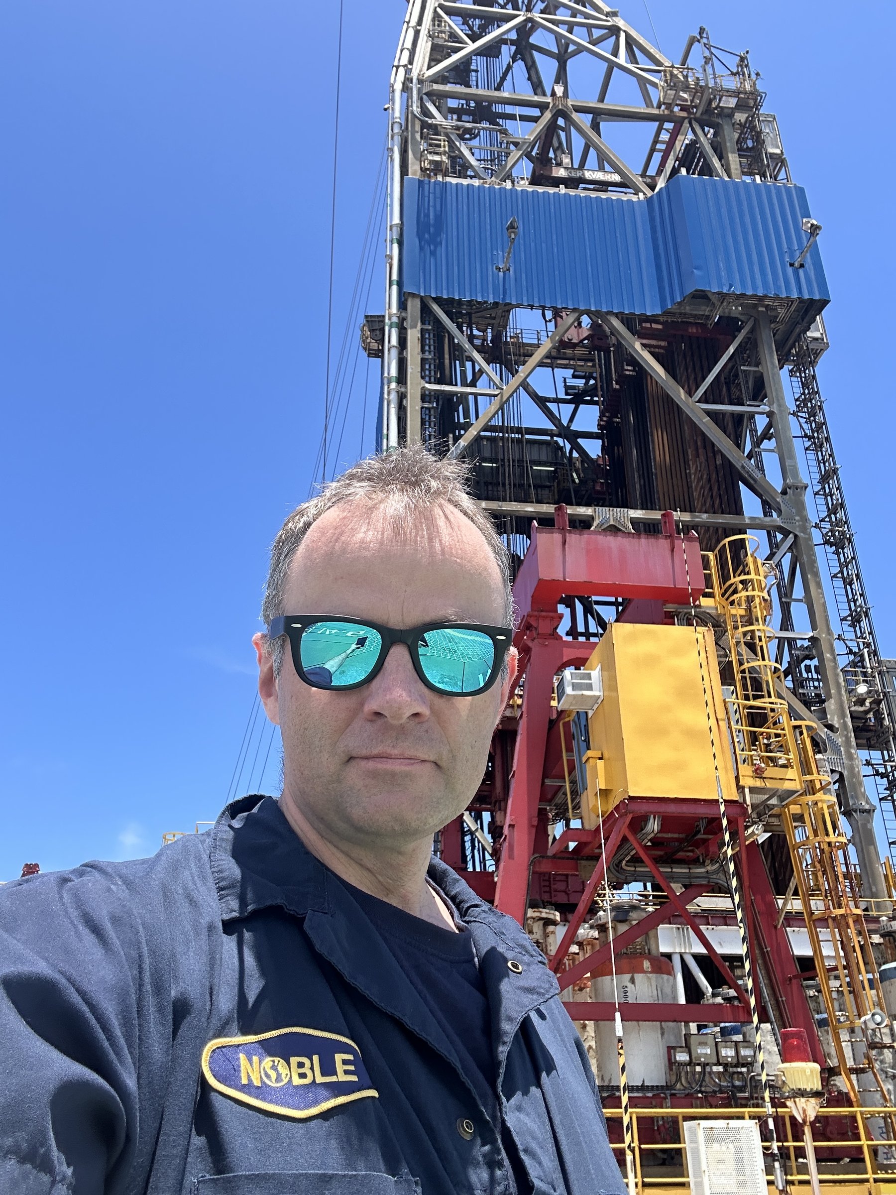 Daniel Czarkowski in coveralls in front of a drilling derrick